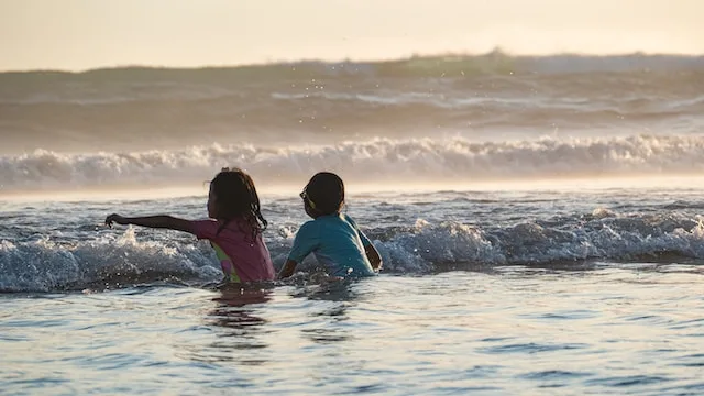 A picture or two kids playing with shallow beach waves - Things to do in Bali with Kids