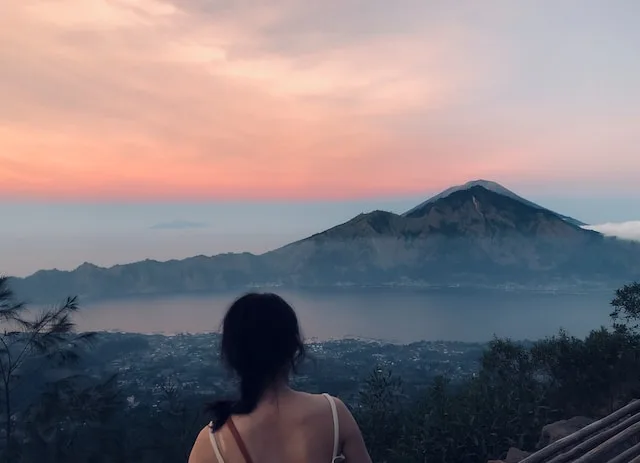 A woman with his back to the camera looking at a view of Mount Batur far away - Things to do in Kintamani