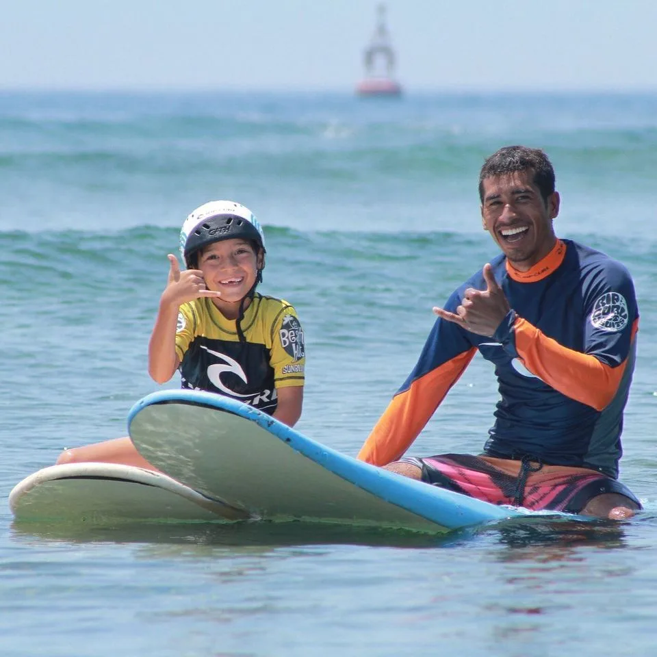 A surfing instructor and a kid with each of their surfing board posing for the camera on the ocean surface