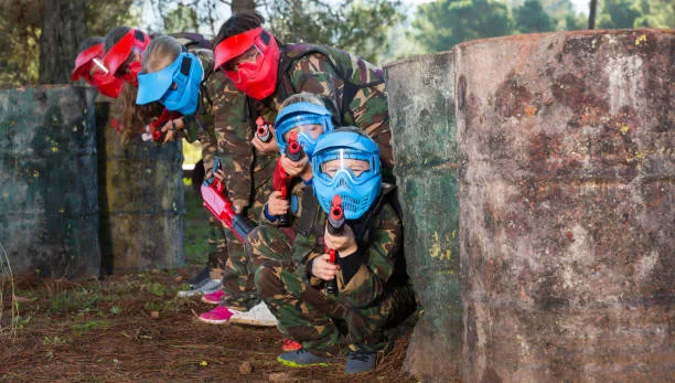 A group of kids armed with paintball atributes crouching beside a low wall