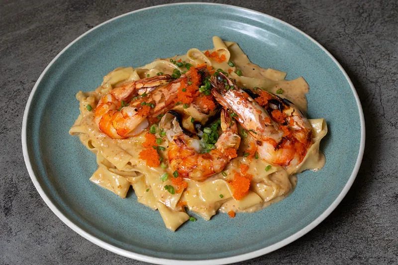 A plate of creamy pasta topped with grilled shrimp, garnished with herbs and orange seasoning