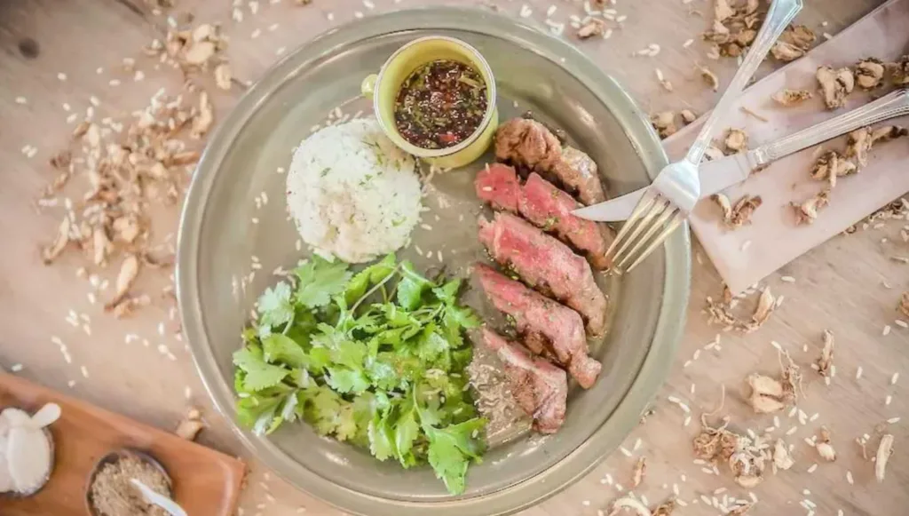 Plate with sliced steak, rice, cilantro, and dipping sauce at Cuca
