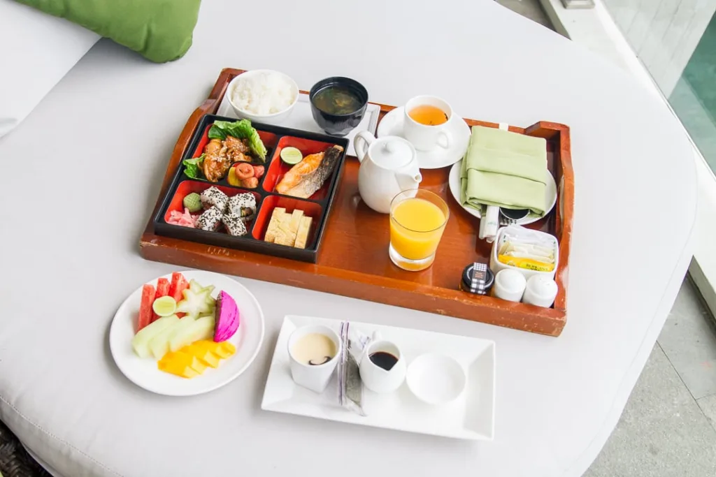 A breakfast set on a tray with fish, rice, soup, and sides, served with fruit, coffee, and juice