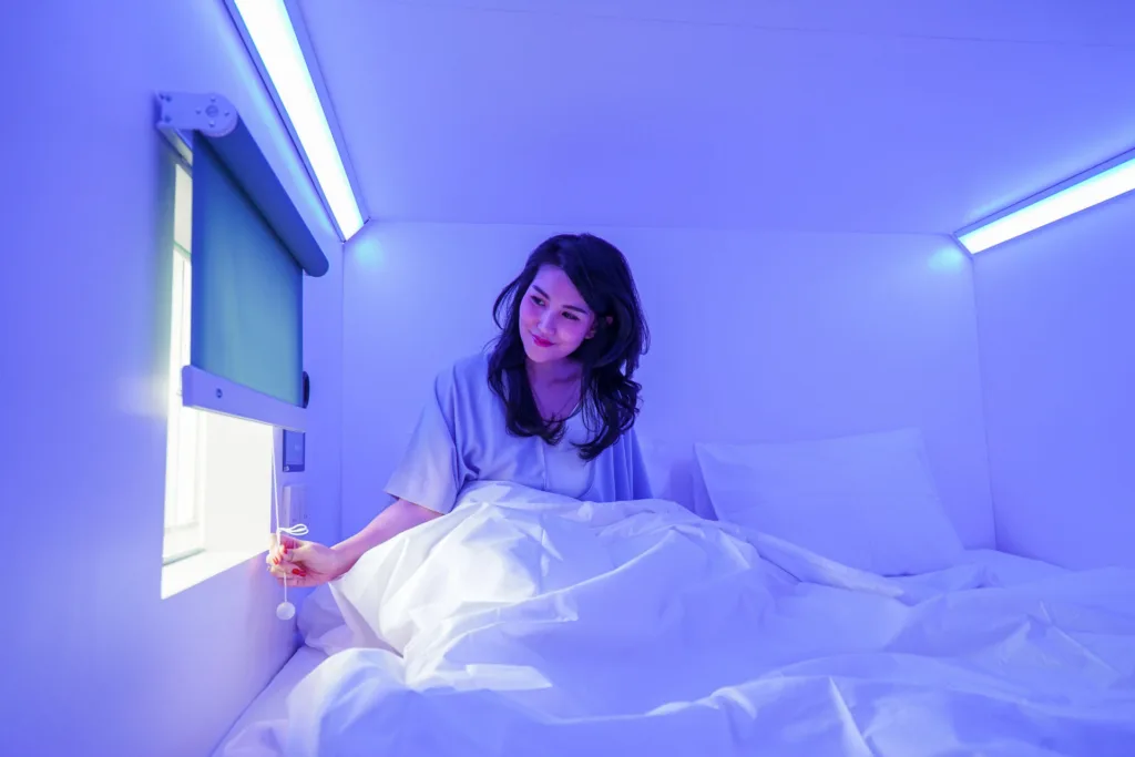 A woman in a capsule hotel pod with purple lighting