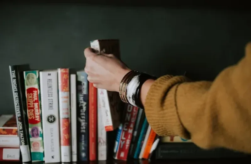 A person's hand reaching out towards books in a shelf